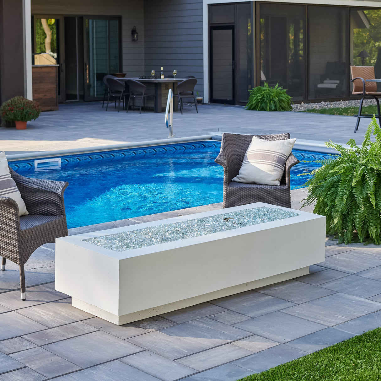 A White Cove Linear Gas Fire Pit Table 72" placed next a pool setup with patio furniture and plants