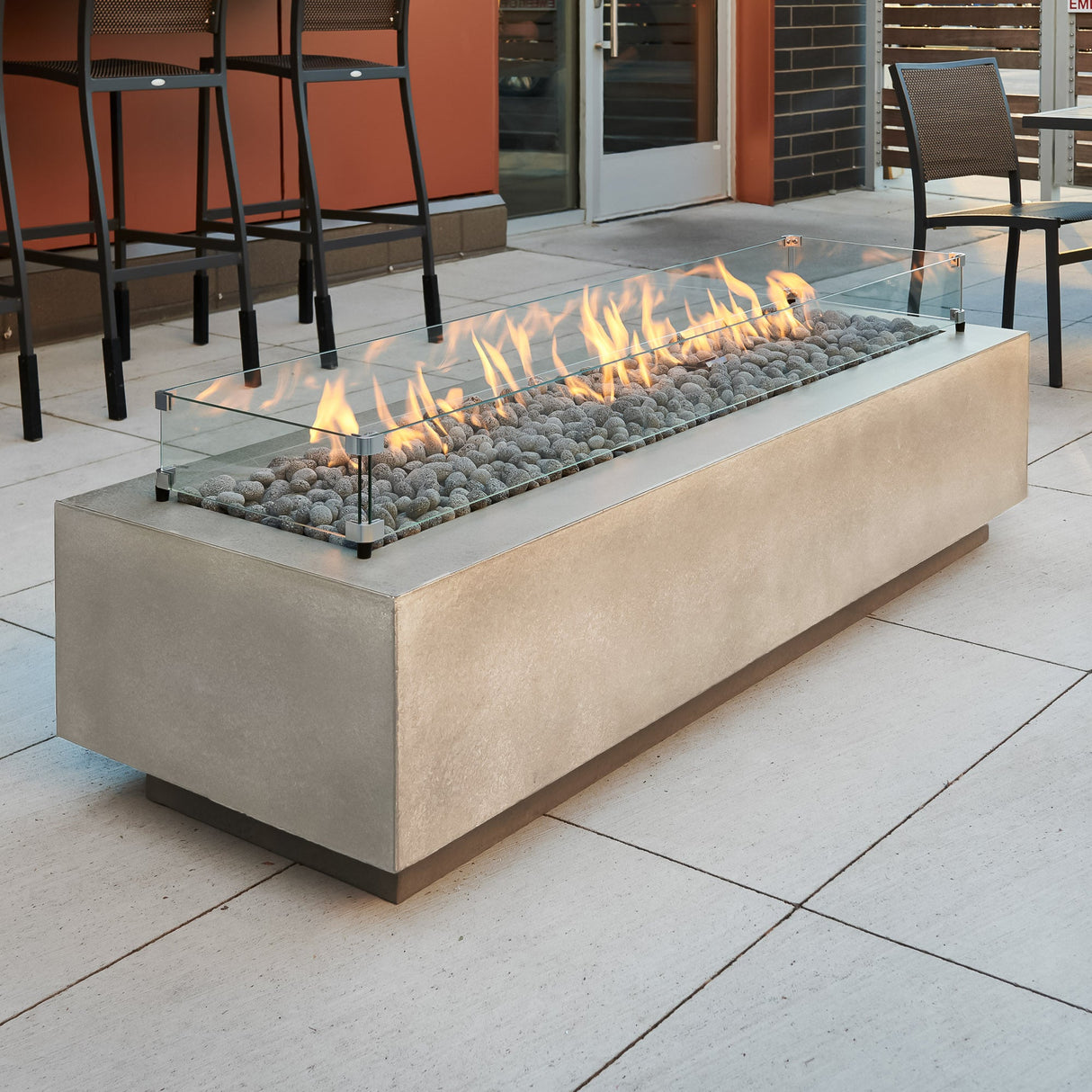 A Natural Grey Cove Linear Gas Fire Pit Table 72" with lava rocks and glass wind guard