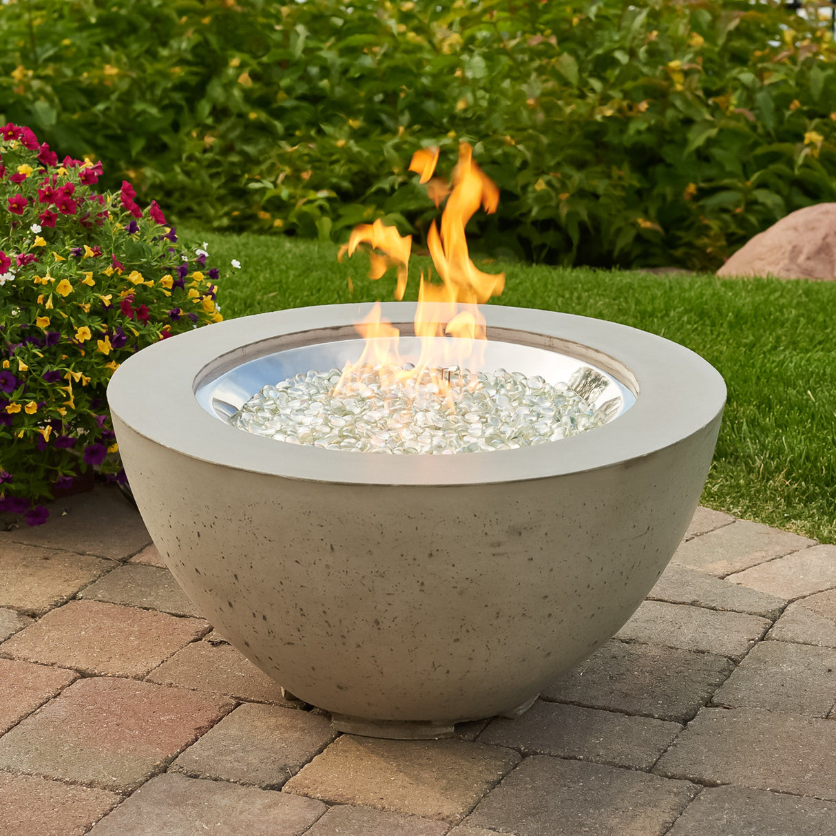 A Cove Round Gas Fire Pit Bowl 29" in a scenic backyard next to flowers