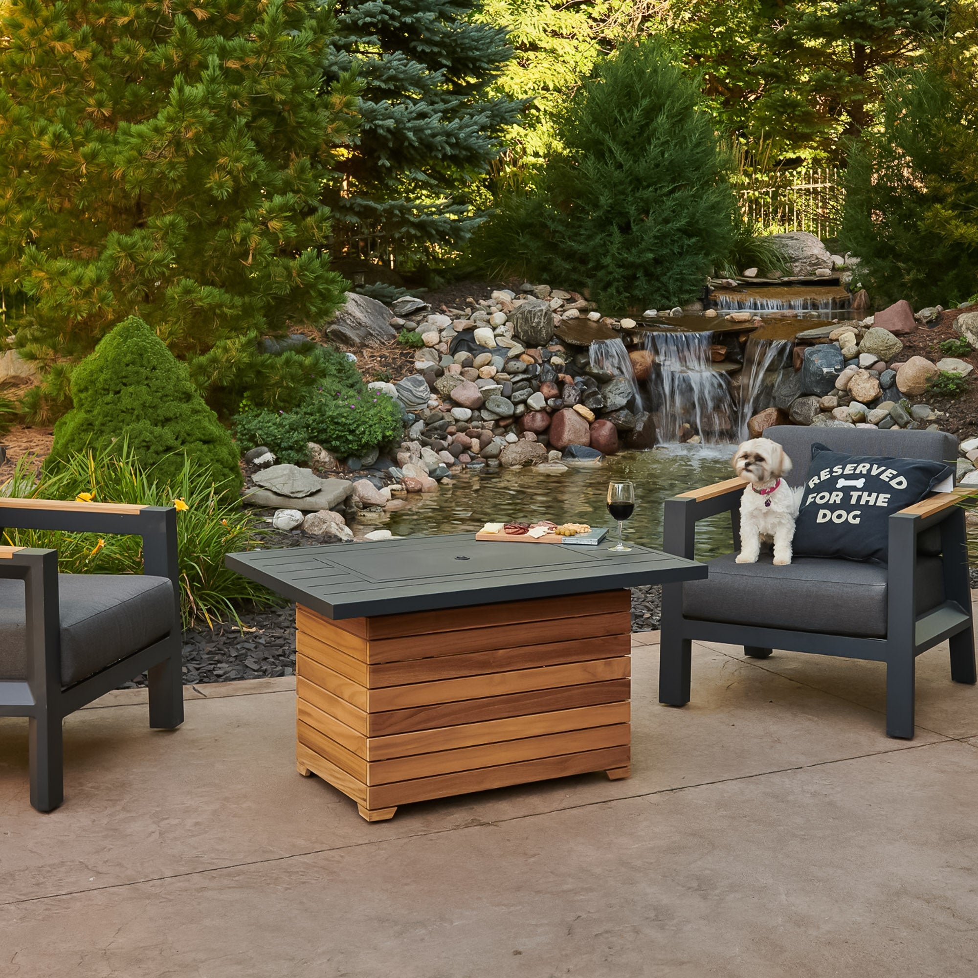 A dog relaxing next to the Darien Rectangular Gas Fire Pit Table being used as table with food and drink on the Aluminum top