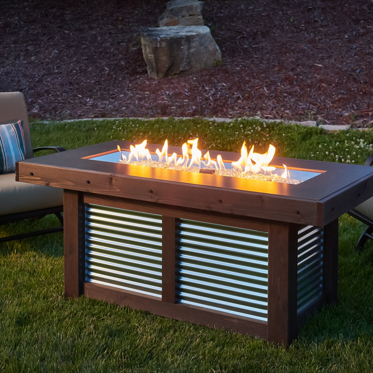 The Denali Brew Linear Gas Fire Pit Table with a large flame and placed in an outdoor backyard space
