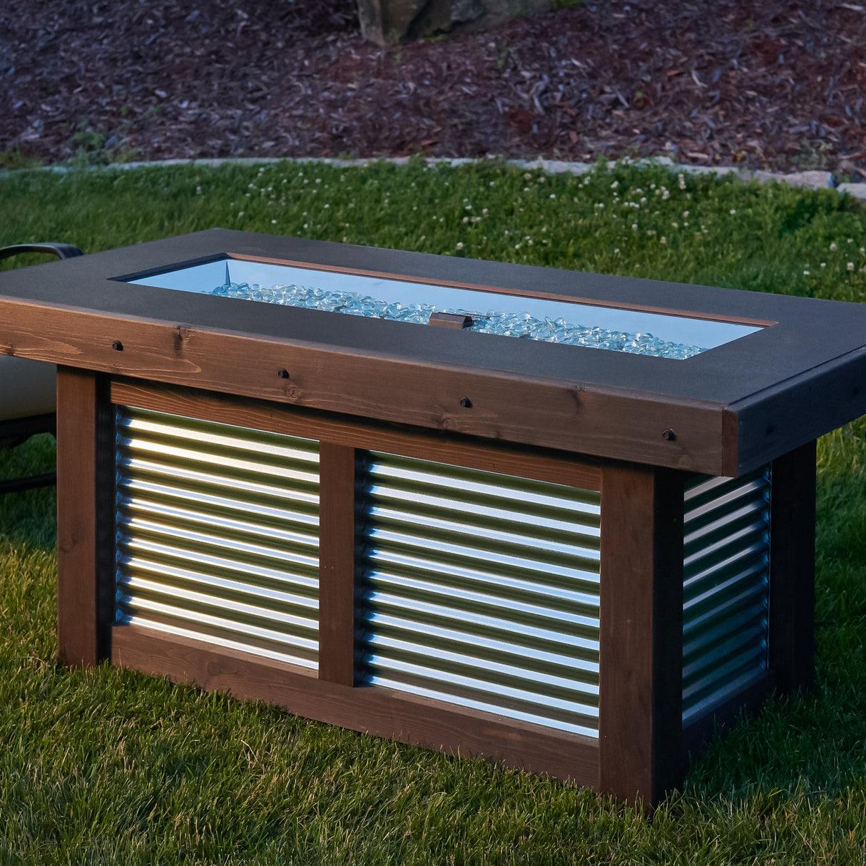 The Denali Brew Linear Gas Fire Pit Table placed on the grass of a backyard