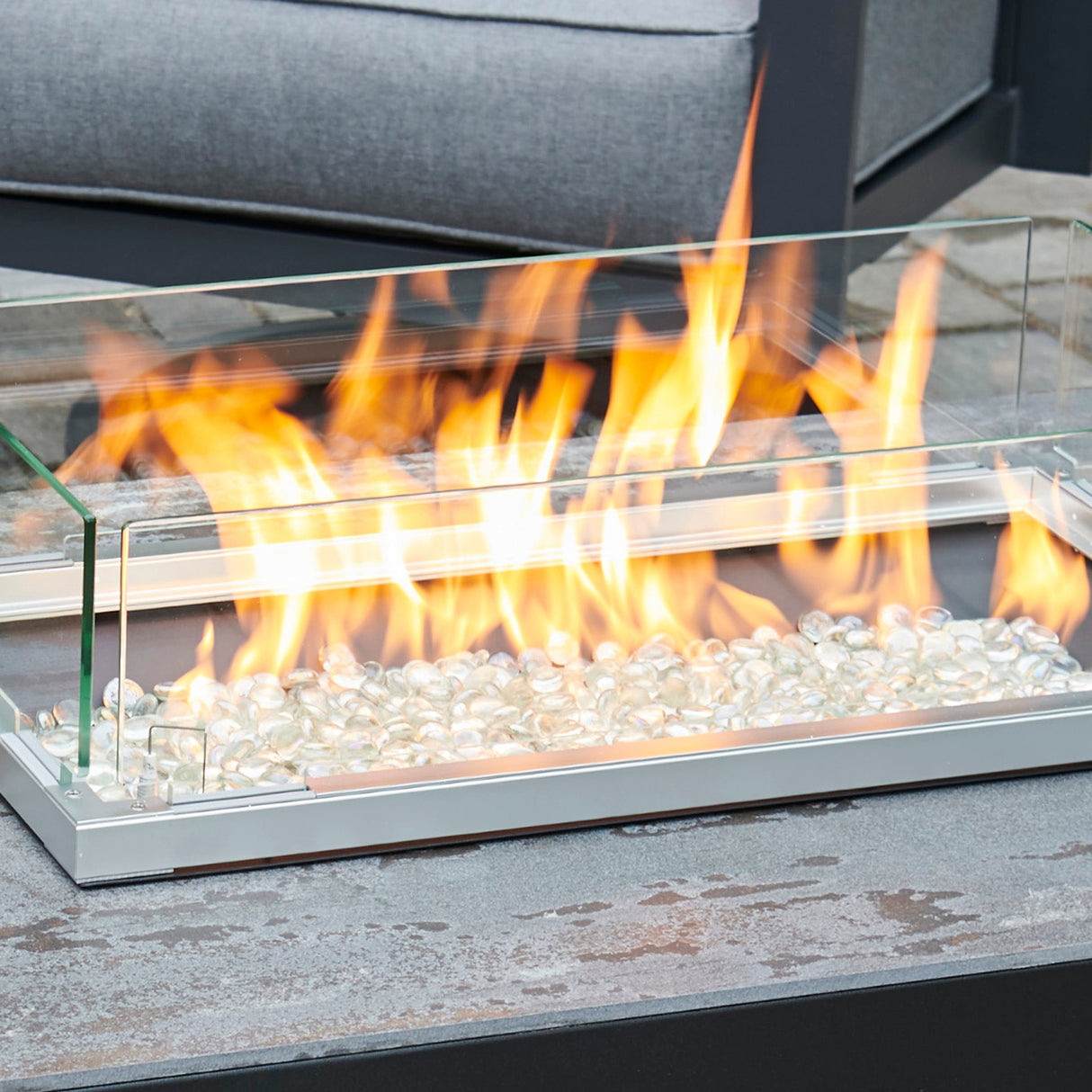 The Linear Folding Glass Wind Guard with a large flame in an outdoor patio setup