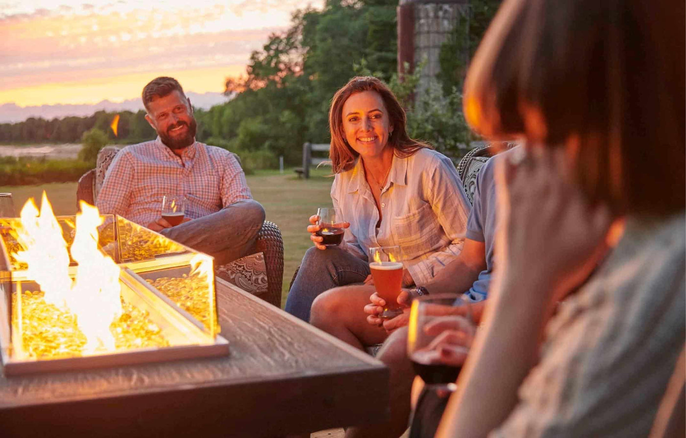 Four individuals enjoying a sunny evening around a Denali Brew Linear Gas Fire Pit Table