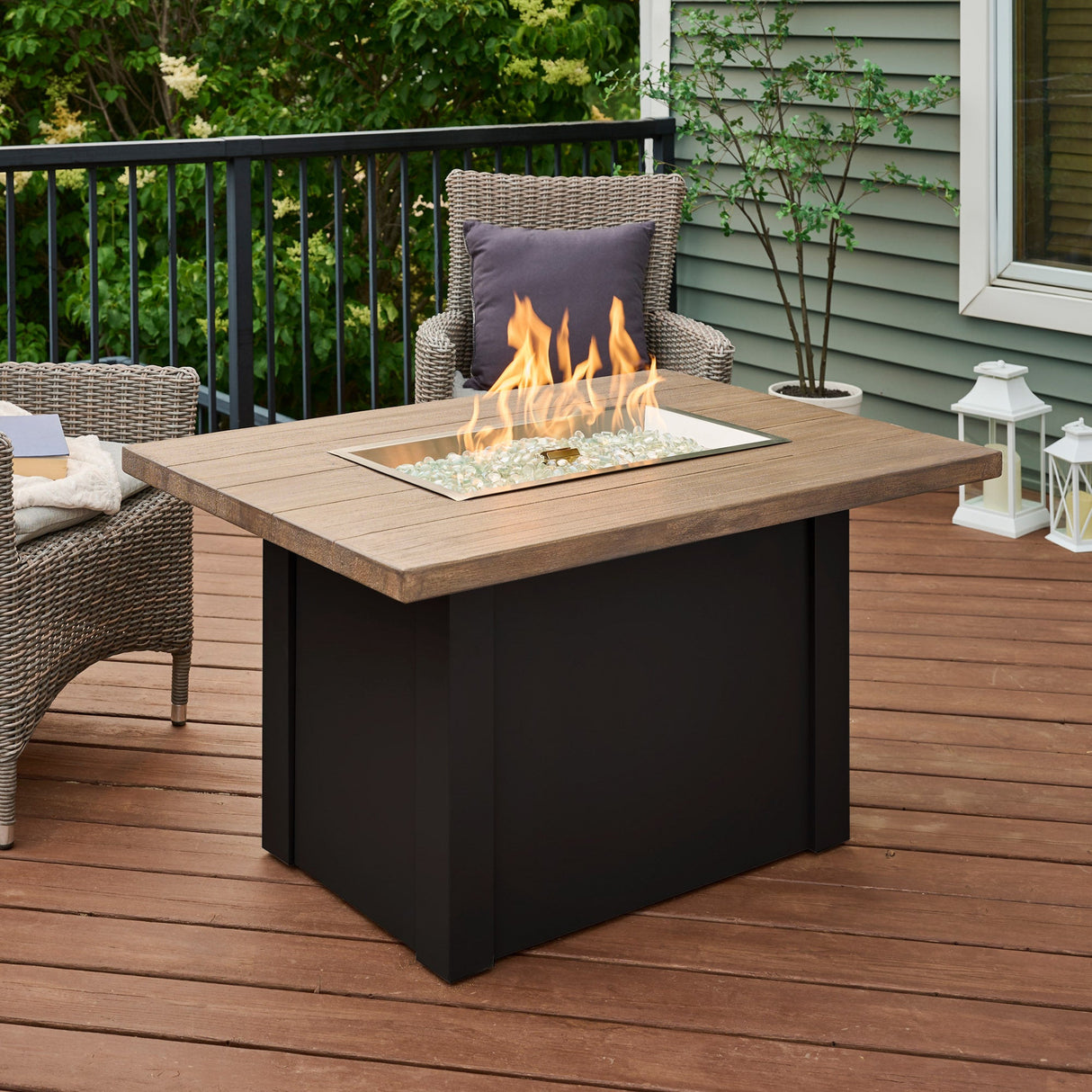 The Havenwood Rectangular Gas Fire Pit Table with a Driftwood top and Luverne Black base on an outdoor patio