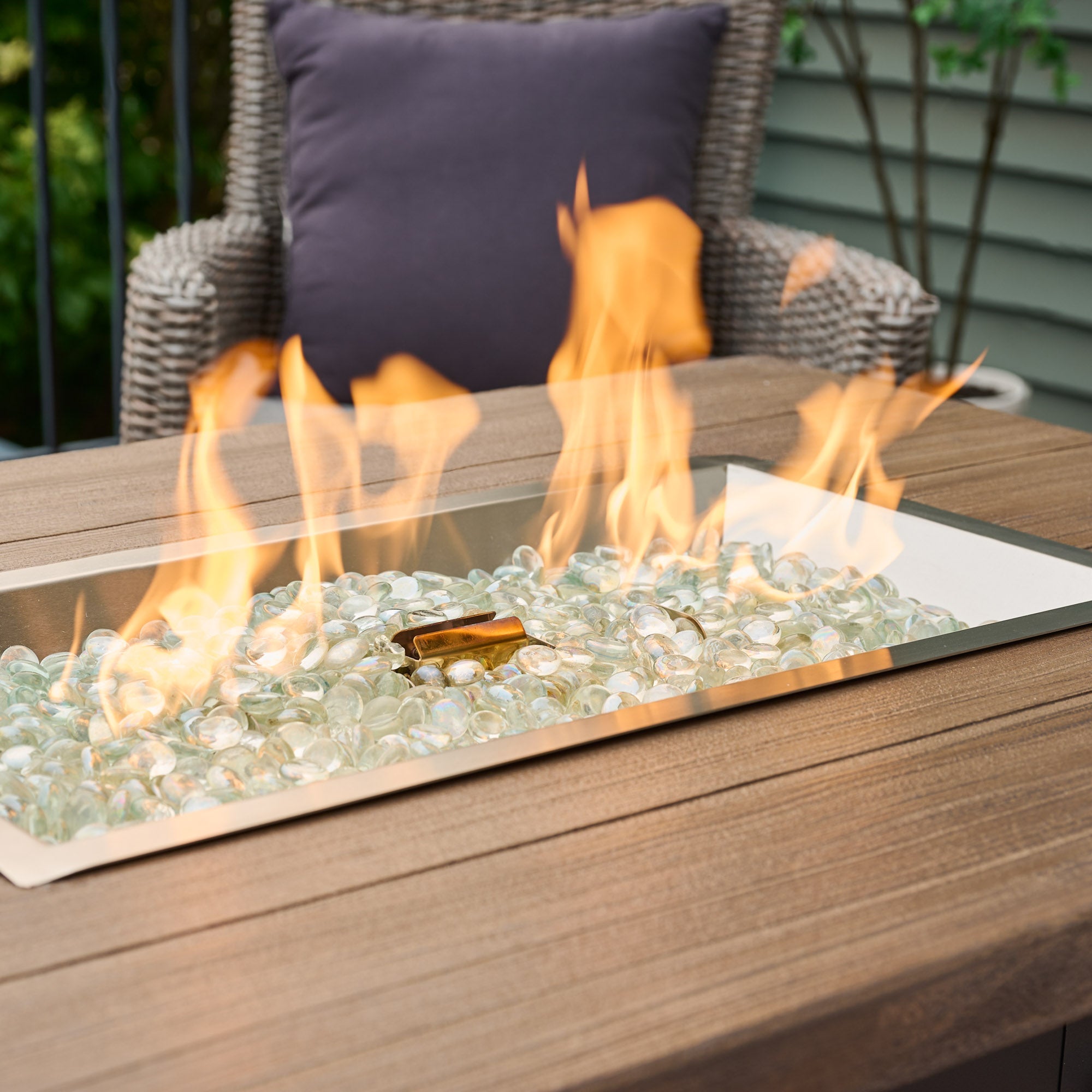 A close up of the flame coming from the burner of a Havenwood Rectangular Gas Fire Pit Table with a Driftwood top and Graphite Grey base