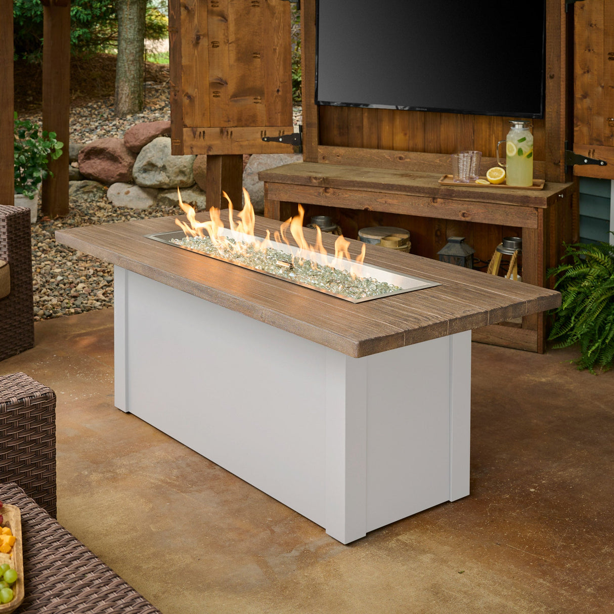 The Havenwood Linear Gas Fire Pit Table with a Driftwood top and White base in a cozy outdoor patio setting