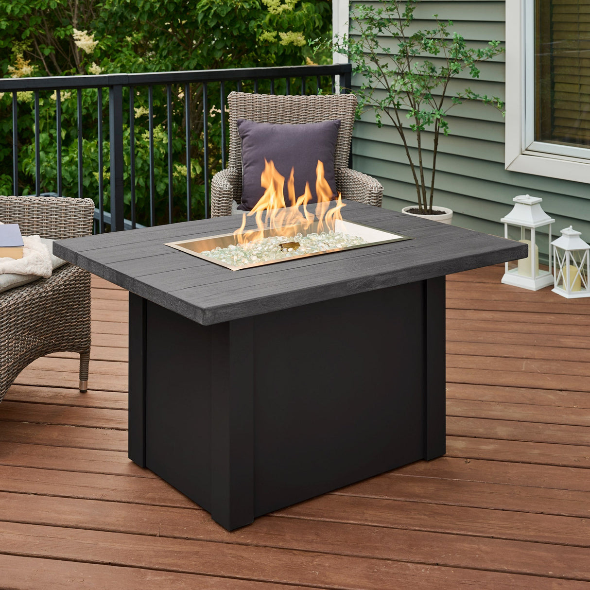 A large flame coming from the burner of a Havenwood Rectangular Gas Fire Pit Table with a Carbon Grey top and Luverne Black base on a patio