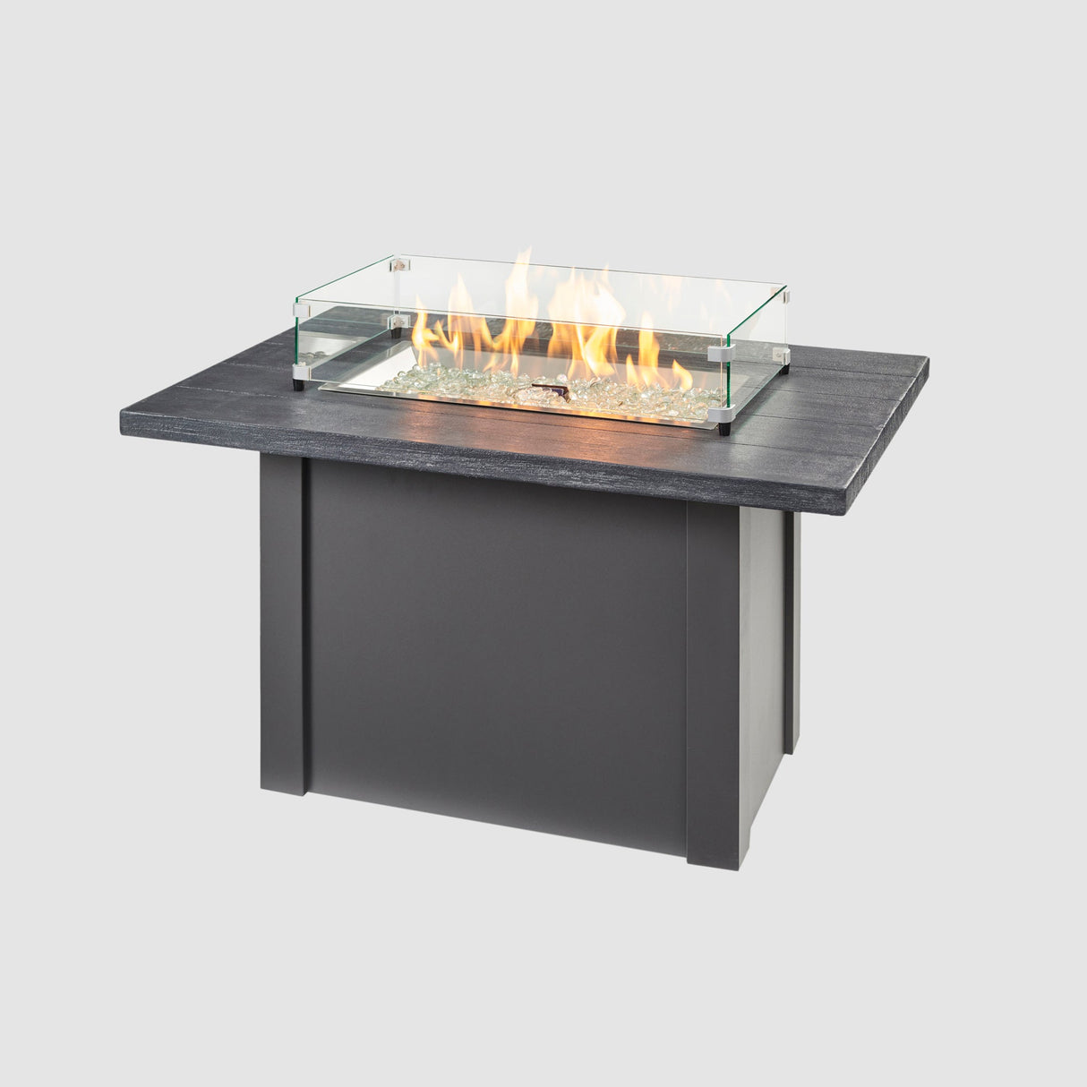 A glass wind guard place around the burner of a Havenwood Rectangular Gas Fire Pit Table with a Carbon Grey top and Graphite Grey base