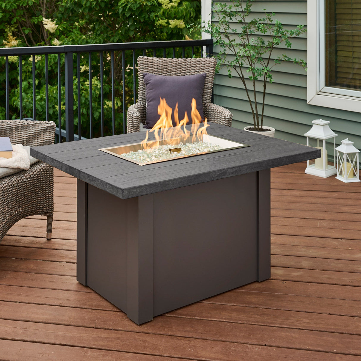 A large flame coming from the burner of a Havenwood Rectangular Gas Fire Pit Table placed in the center of an outdoor deck
