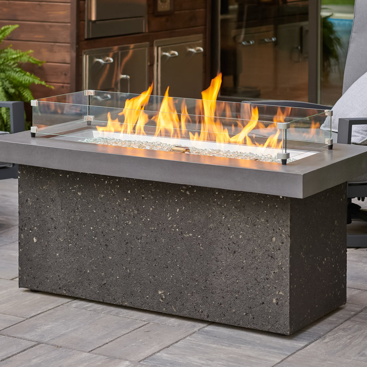 Close up of the Midnight Mist Key Largo Linear Gas Fire Pit Table with a glass wind guard being used to protect the flame