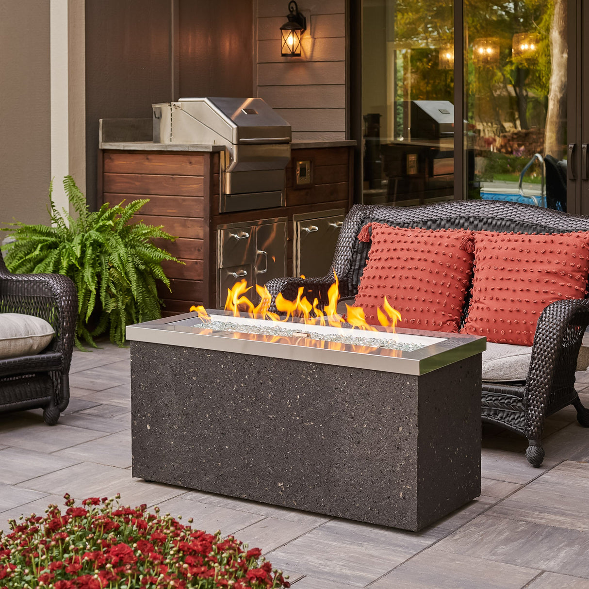 Stainless Steel Key Largo Linear Gas Fire Pit Table placed on a patio with a nice flame coming from the burner