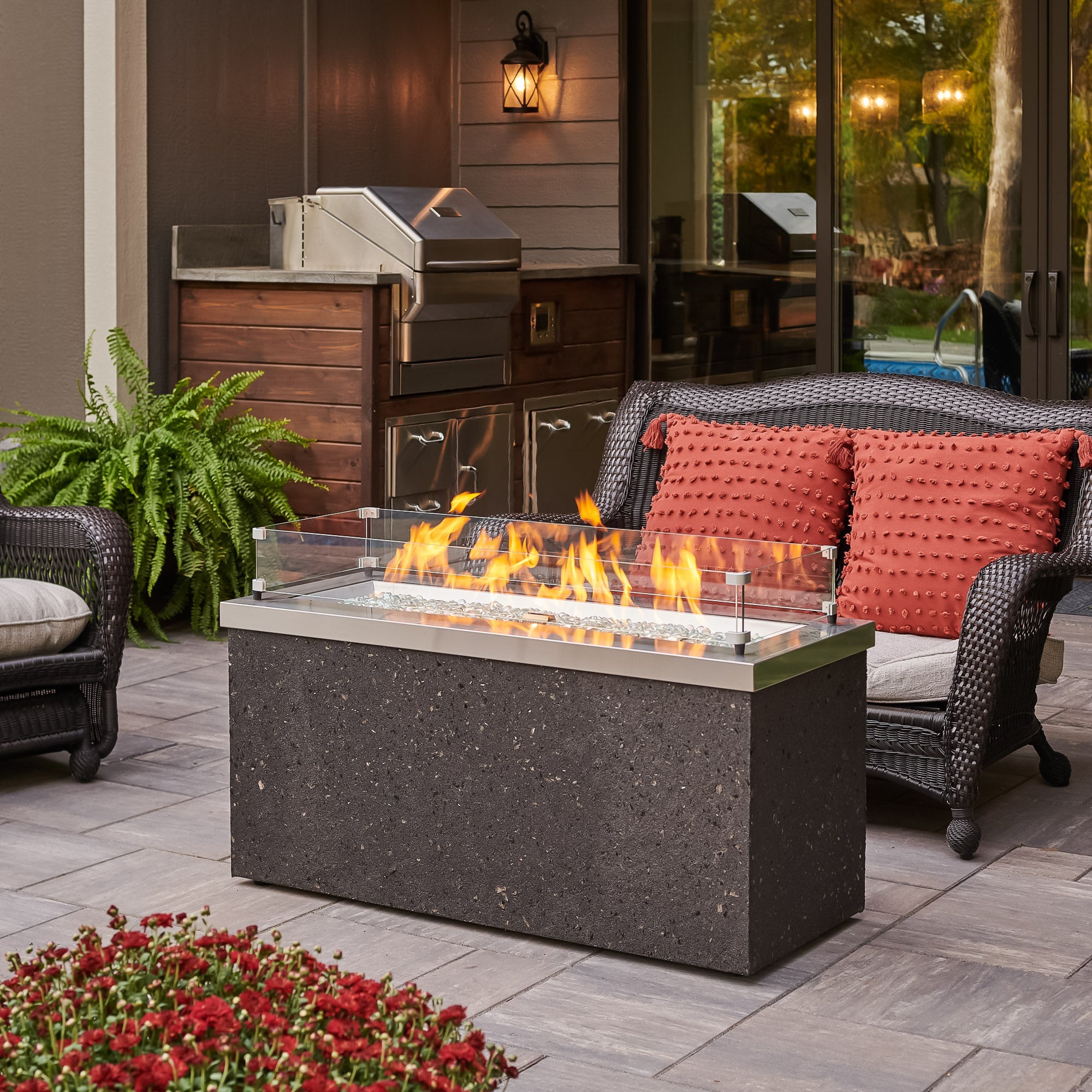 A glass wind guard being used on the Stainless Steel Key Largo Linear Gas Fire Pit Table to protect the flame from the wind