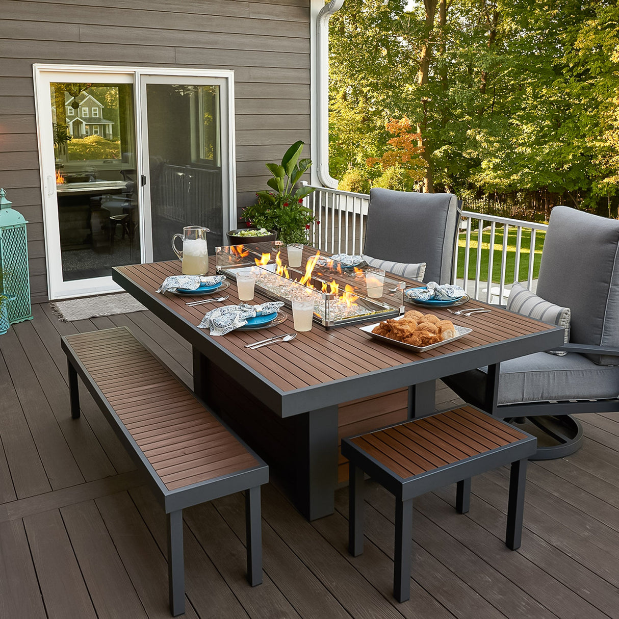 Food and drink placed around the top of the Kenwood Linear Dining Height Gas Fire Pit Table on an outdoor patio setup