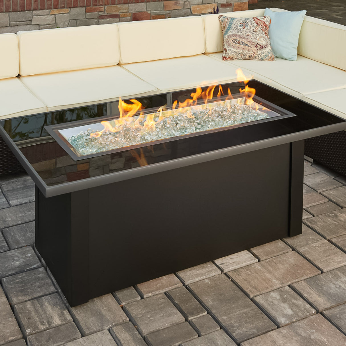The Monte Carlo Linear Gas Fire Pit Table placed around an outdoor couch on a patio setting