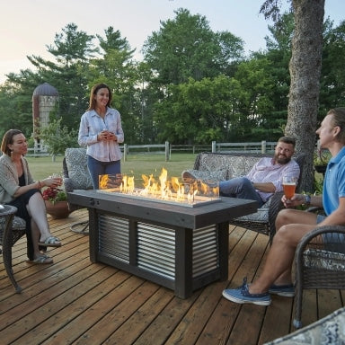 Four individuals on an outdoor deck that features a Denali Brew Linear Gas Fire Pit Table