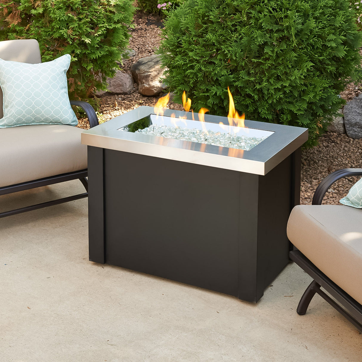 The Providence Rectangular Gas Fire Pit Table placed on a patio with furniture surrounding it