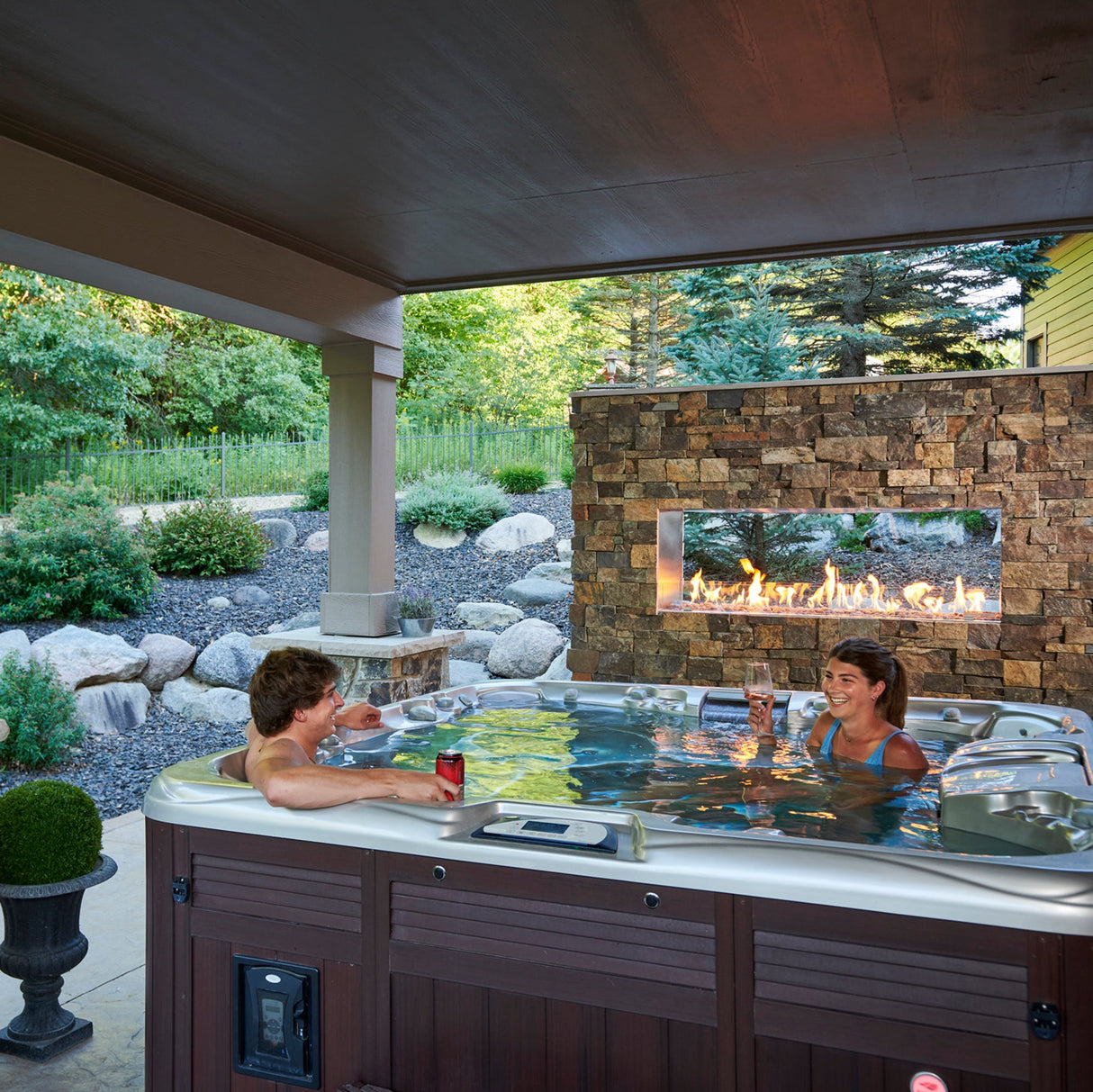 Two individuals in a hot tub next to their See Through Ready to Finish Gas Fireplace on a grey background