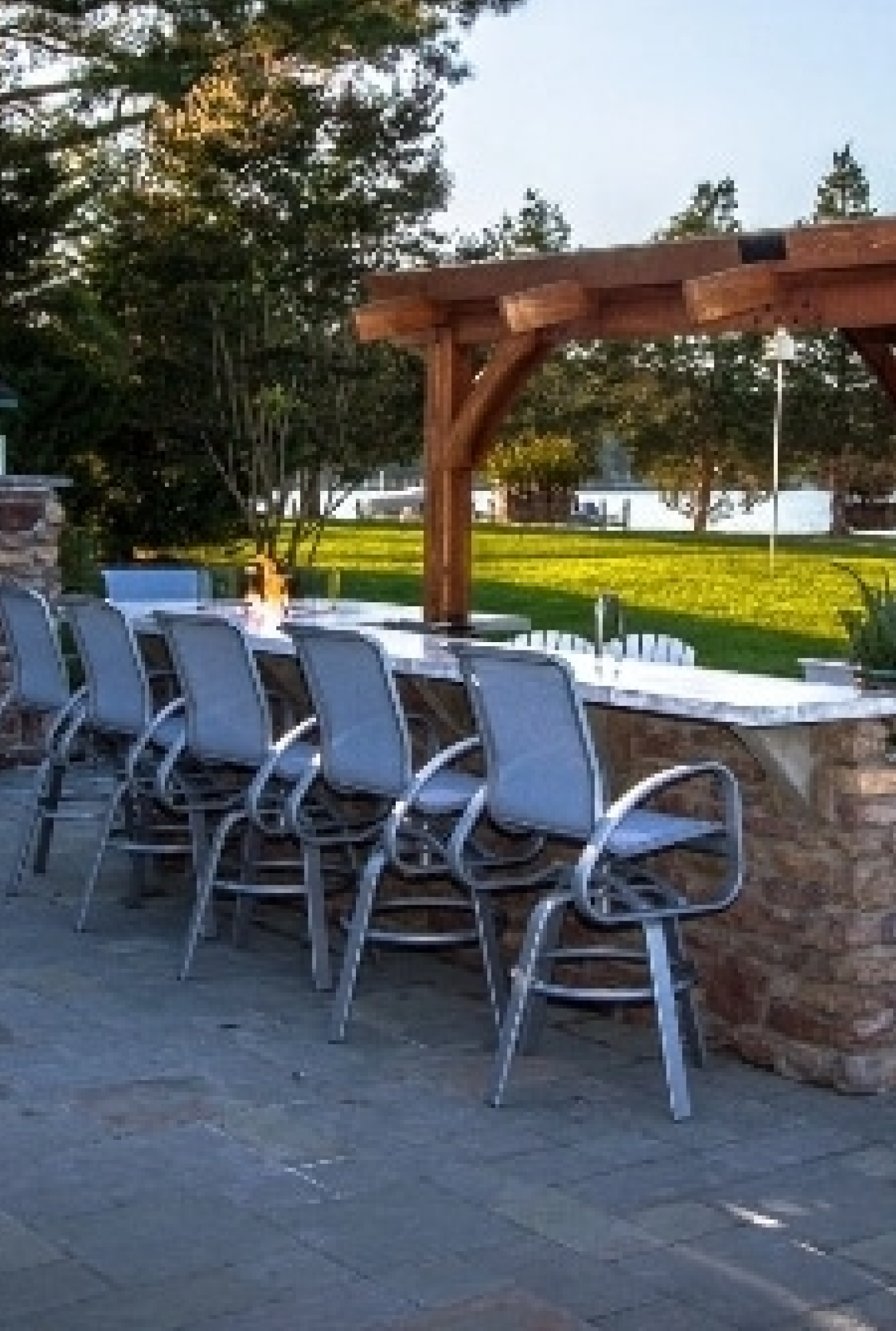 A row of outdoor patio chairs next to a sprawling pergola and custom outdoor kitchen setup
