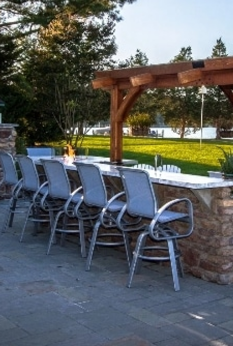 A row of outdoor patio chairs next to a sprawling pergola and custom outdoor kitchen setup