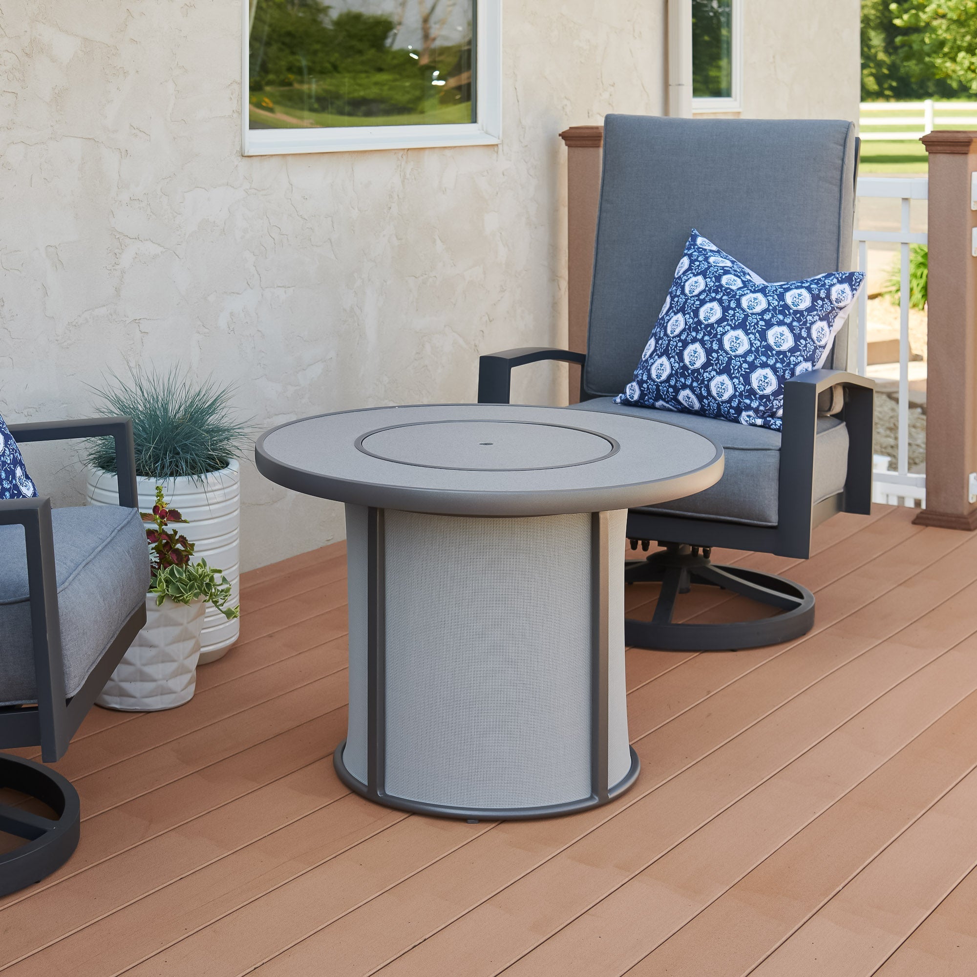 A cover placed on the Grey Stonefire Round Gas Fire Pit Table next to some patio furniture