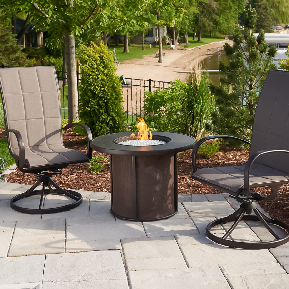 The Brown Stonefire Round Gas Fire Pit Table next to a beach surrounded by patio furniture