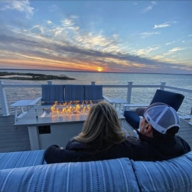 Two individuals sitting next to each other on an outdoor couch next to a linear gas fire pit table