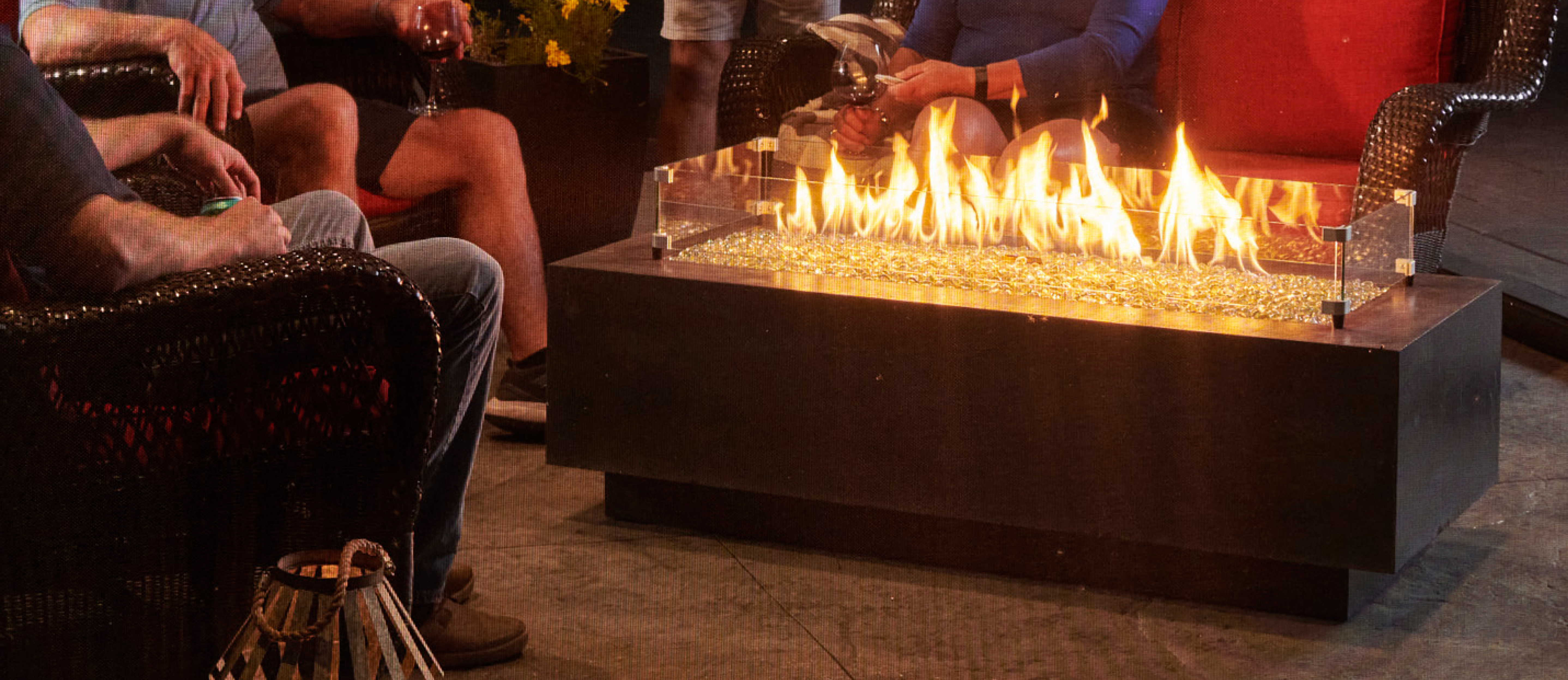 Individuals gathered around a midnight mist Cove Linear Gas Fire Pit Table in a screened in porch