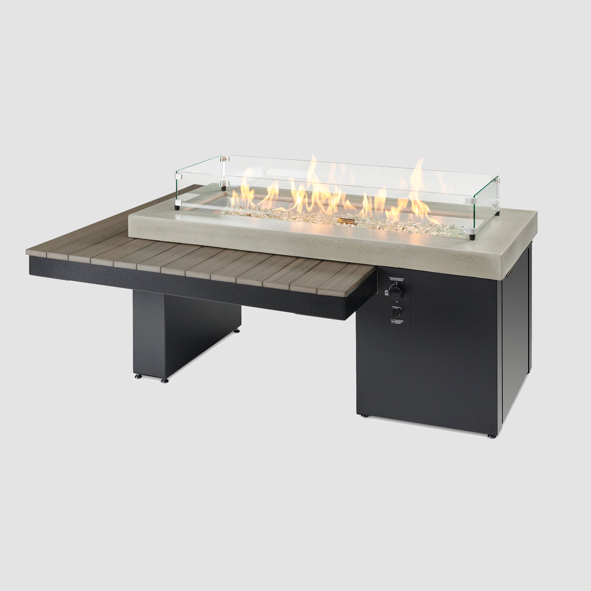 The Uptown Coastal Grey Linear Gas Fire Pit Table with flame and glass wind guard.