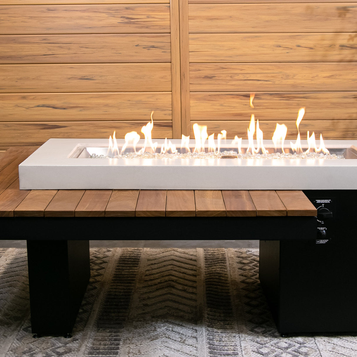 The Uptown Iroko Linear Gas Fire Pit Table placed near a wooden background