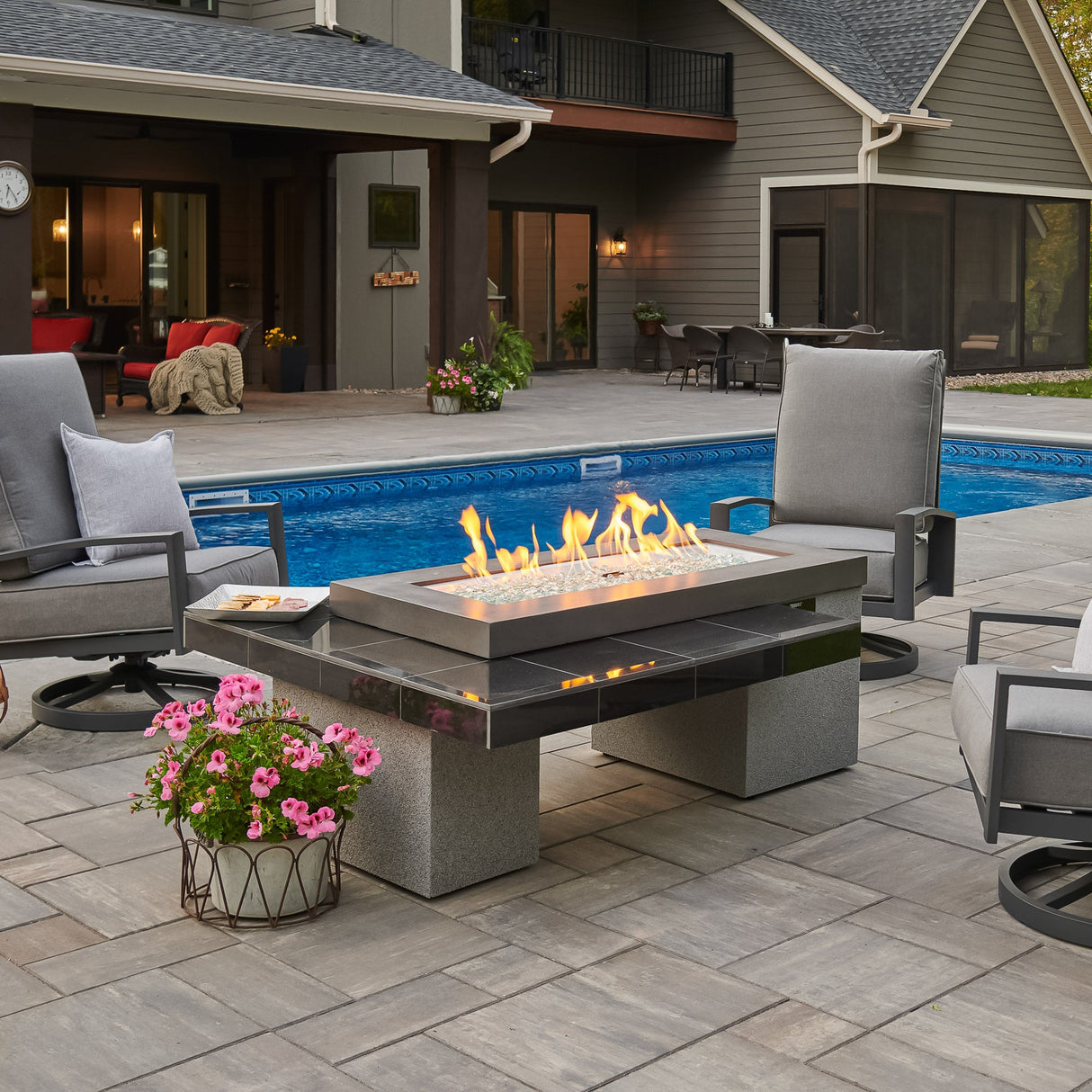 The Black Uptown Linear Gas Fire Pit Table next to a pool and surrounded by patio furniture