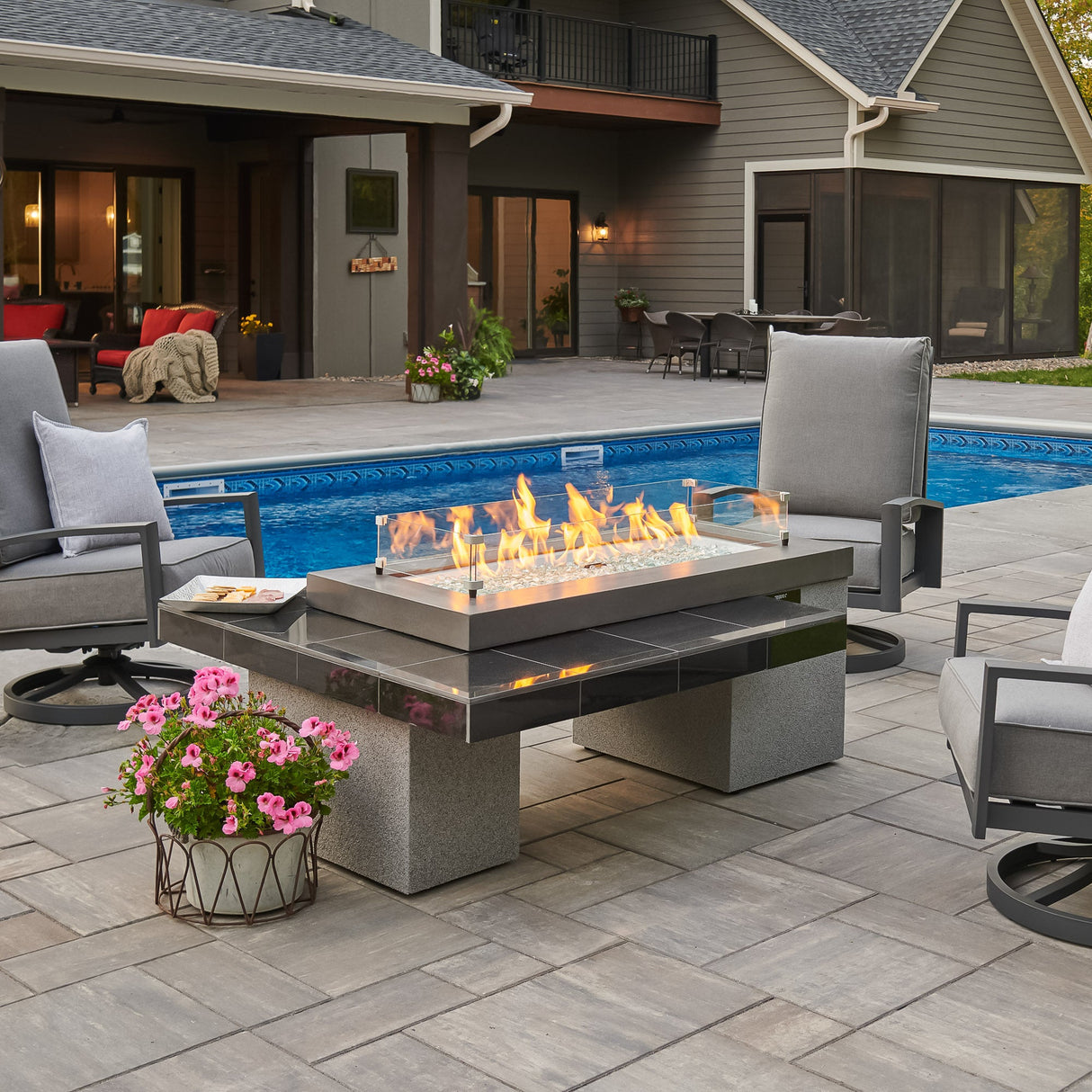 A glass wind guard placed on the top of a Black Uptown Linear Gas Fire Pit Table next to a pool