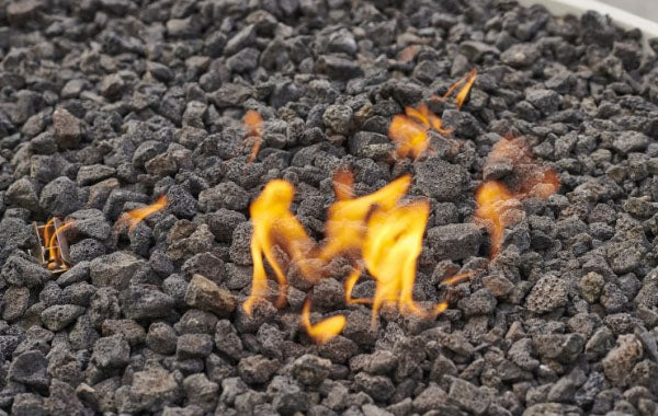 A close up view of lava rocks on a burner with a large flame