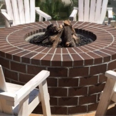 A brick fire pit surrounded by white patio furniture on a patio