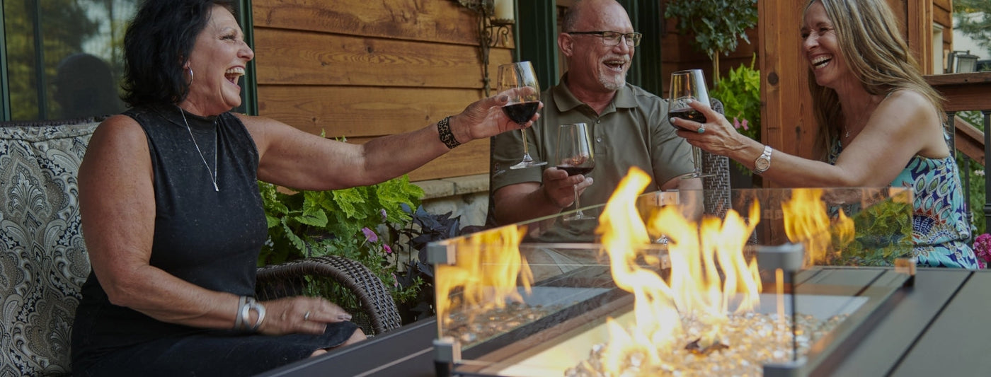 Three older individuals sharing a drink around a fire pit table