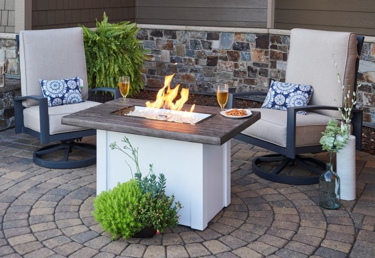 A Havenwood Rectangular Gas Fire Pit Table with food and drink on the top surrounded by patio furniture