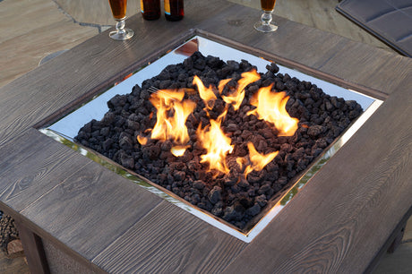 A close up view of black lava rock in a fire pit table on a patio setup