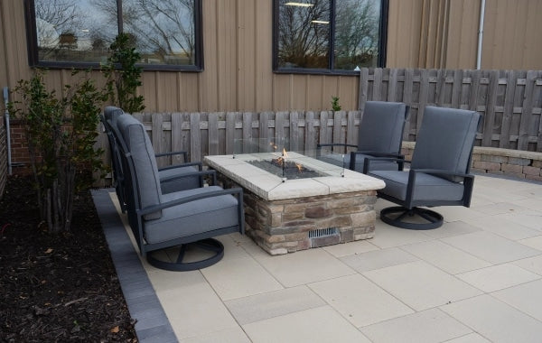 A linear gas fire pit table with a glass wind guard on its top